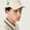 Cappellino da baseball color crema con toppa tono su tono “Golden” e spilla a forma di stella verde